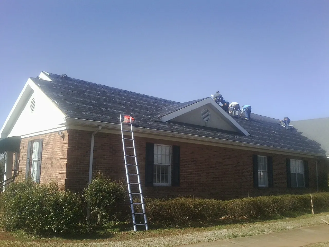 Crew tearing shingles off a brick ranch roof with a ladder set — Emergency Roof Repair work by our crew in Mahopac