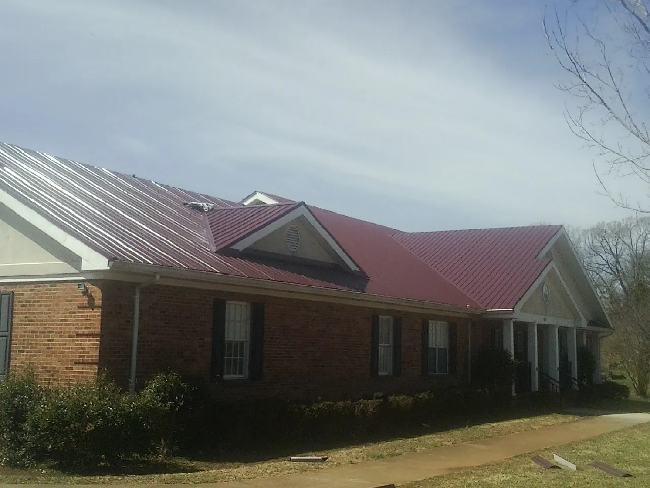 Red metal roof with gabled entries on a long brick building, from a Hail Damage Roof Repair job in Mahopac
