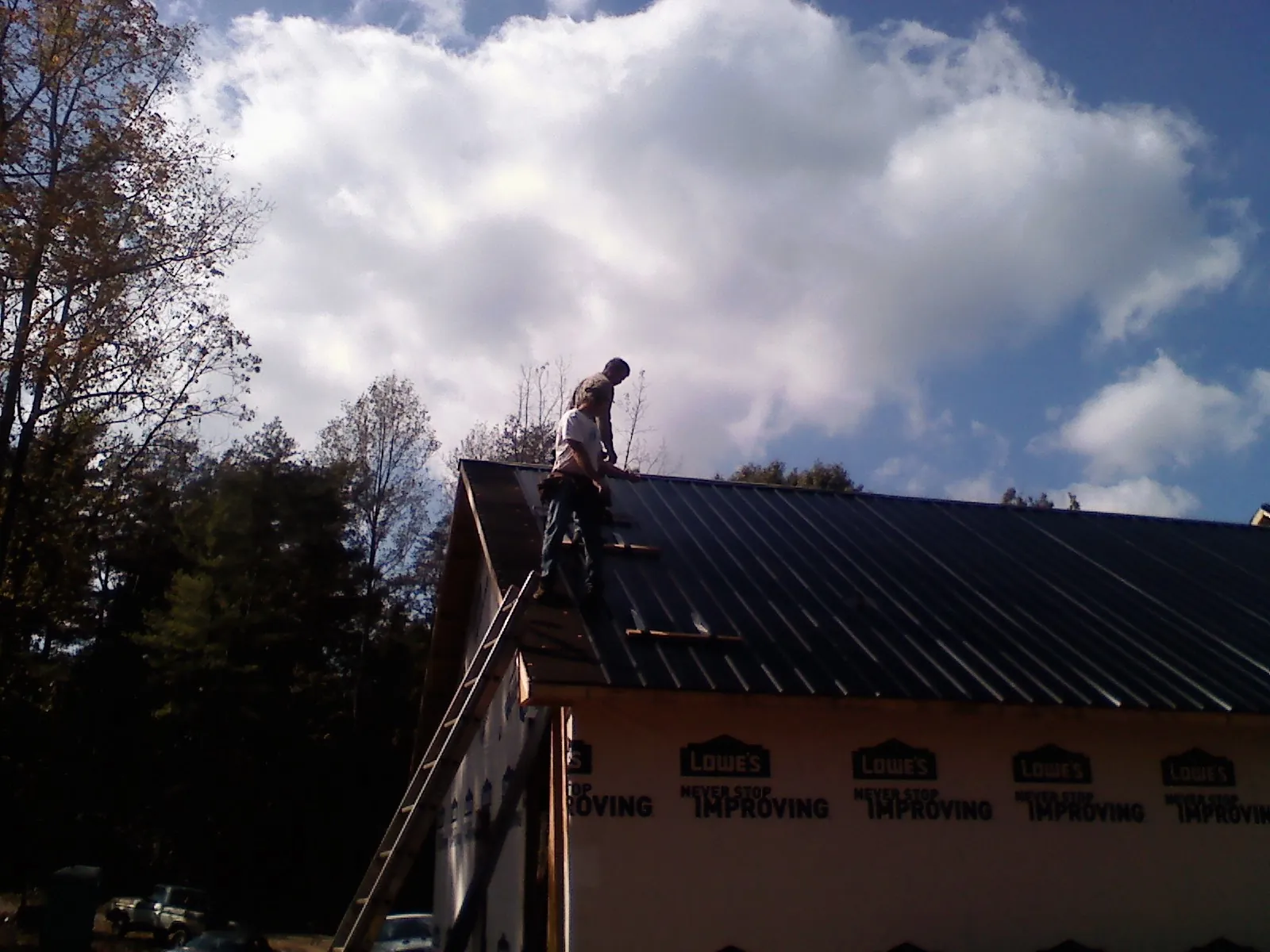 Roofer fastening dark metal panels high against a cloudy sky, from a Roof Inspection job in Mahopac