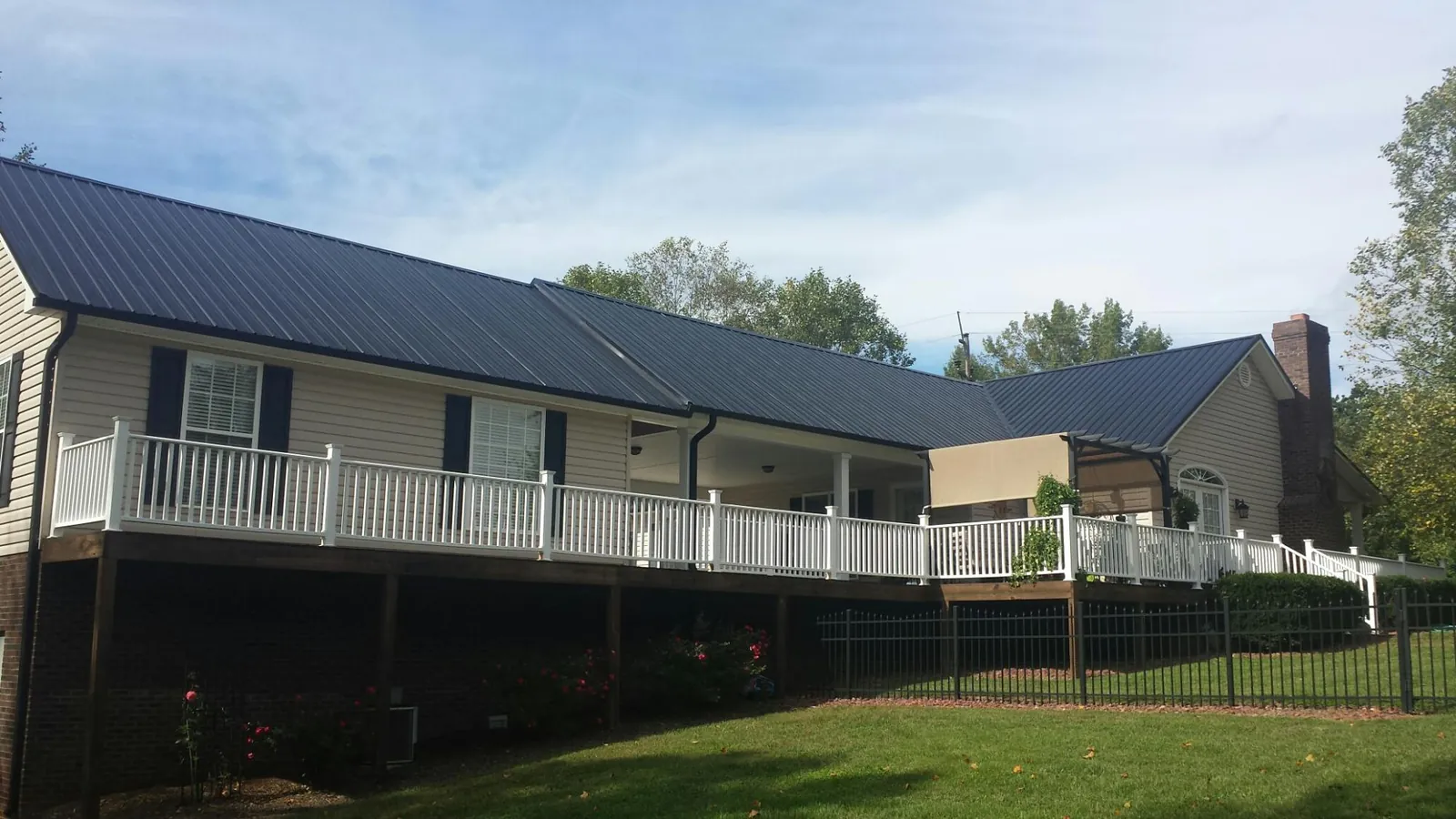 Black metal roof above a long white railed deck on a hillside home in Mahopac