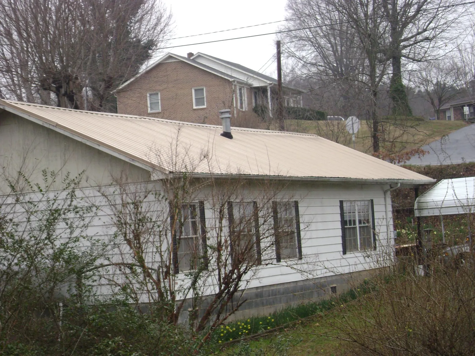 Tan metal roof on a white sided house set into a hillside — Commercial Roofing by Roofing Brothers in Mahopac